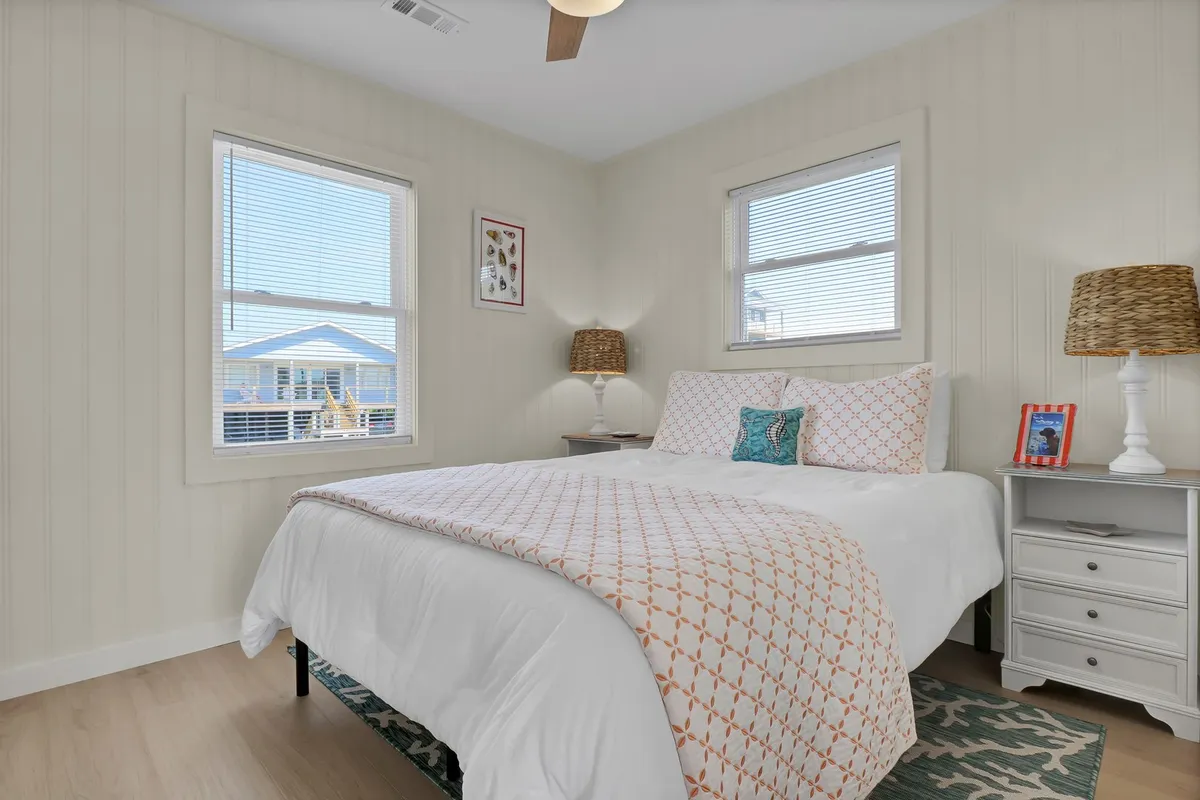 A cozy bedroom featuring a comfortable bed with patterned bedding, side tables with lamps, and abundant natural light glowing through the windows. The atmosphere is inviting and serene, perfect for restful sleep.