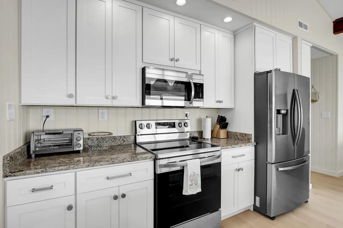 A modern kitchen featuring gleaming stainless steel appliances, a granite countertop, and crisp white cabinetry. The counters are clear and spacious, inviting both cooking and socializing, while the overall look is clean, fresh, and newly updated.