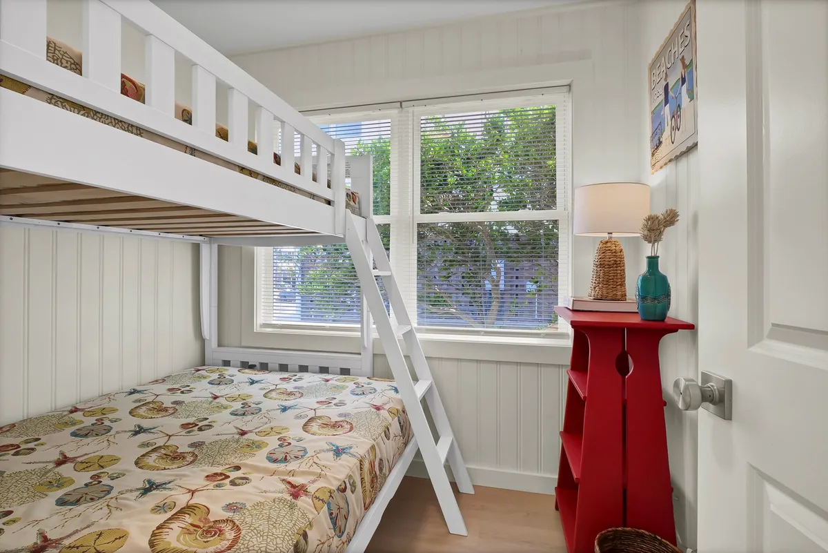 A playful bedroom with a twin-over-full bunk bed dressed in colorful bedding, accented by bold red furniture and a cheerful lamp. The space feels fun and welcoming—ideal for children or groups of friends.